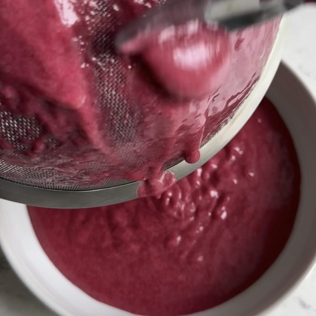 Running blackberry curd into a sieve to get a smooth texture