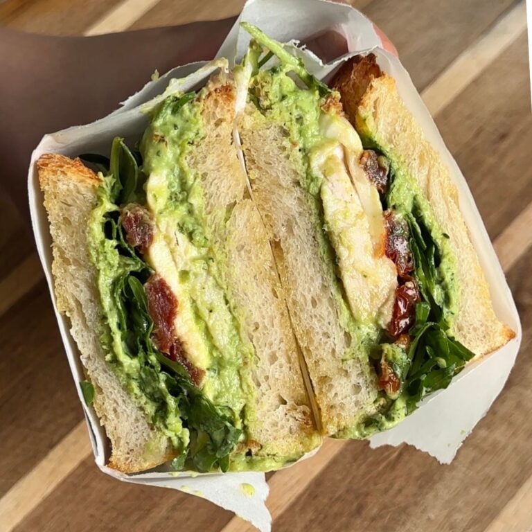mint pea and ricotta chicken sandwich cut in half exposing the filling where there is the green sauce, rocket, sun dried tomatoes, and chicken