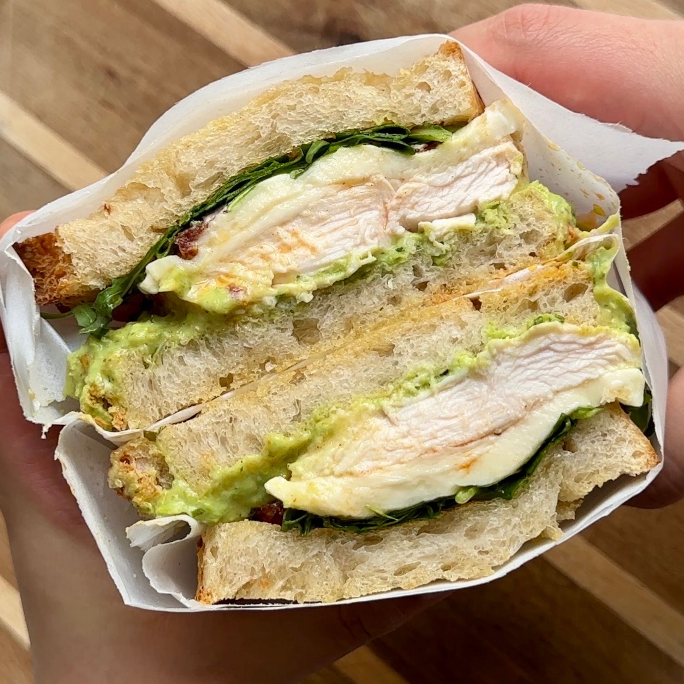 mint pea and ricotta chicken sandwich cut in half exposing the filling where there is the green sauce, rocket, sun dried tomatoes, and chicken