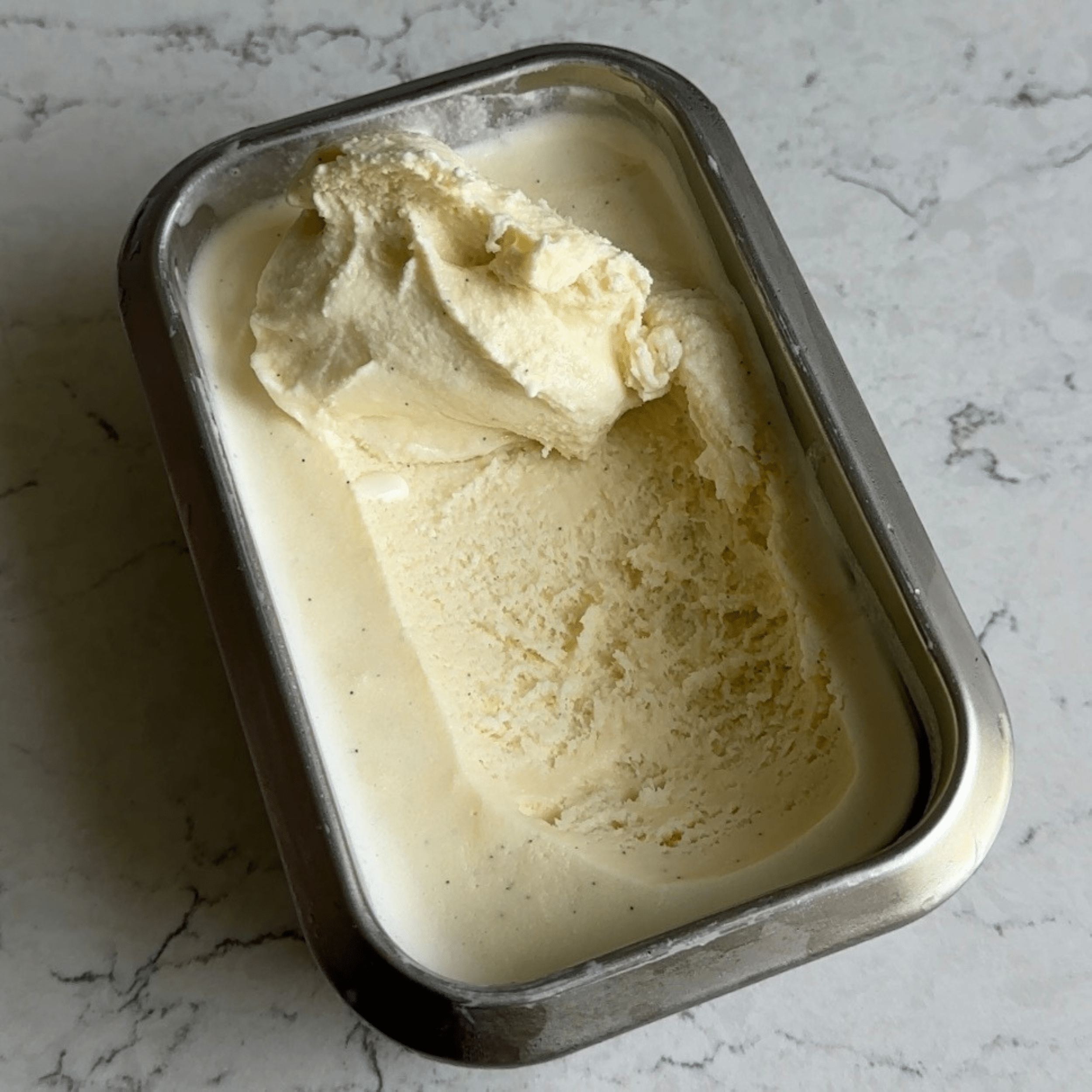 Vanilla ice cream in a metal container with a scoop at the top to show the texture of the ice cream